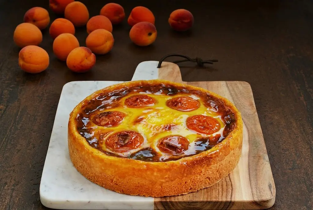 Flan abricot vanille fraîchement préparée avec texture crémeuse, abricots brillants nappés et base croustillante aux amandes sur une assiette élégante.